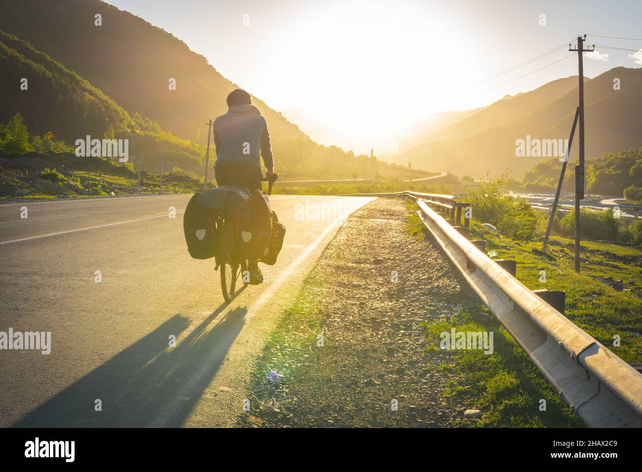Immagine di sfondo creativa di un turista in bicicletta sulla strada di campagna con il tramonto in montagna su strada vuota. Tour in bicicletta autonomo. Ecolo Foto Stock