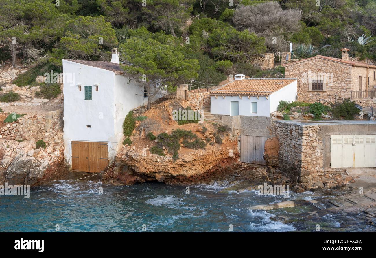 Paesaggio della costa rocciosa dell'isola di Maiorca, con un villaggio di pescatori costiero, una giornata invernale nuvolosa e soleggiata. Baia di S'Almonia Foto Stock