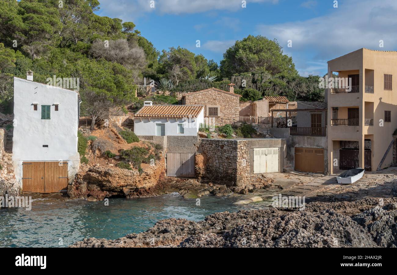 Paesaggio della costa rocciosa dell'isola di Maiorca, con un villaggio di pescatori costiero, una giornata invernale nuvolosa e soleggiata. Baia di S'Almonia Foto Stock
