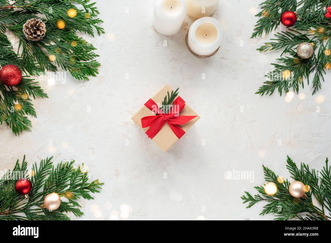 Scatola regalo di Natale, decorata con nastro rosso. Rami di abete, candele e palline di Natale su sfondo bianco testurizzato. Vista dall'alto, piatto Foto Stock