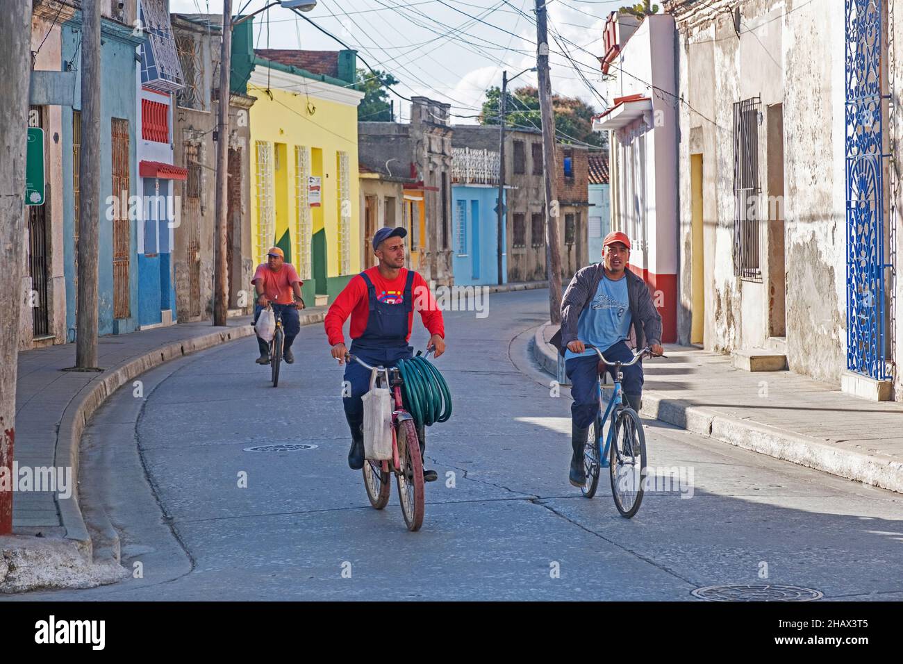 Uomini cubani che cavalcano in bicicletta attraverso la strada colorata nel centro storico della città Camagüey sull'isola Cuba, Caraibi Foto Stock