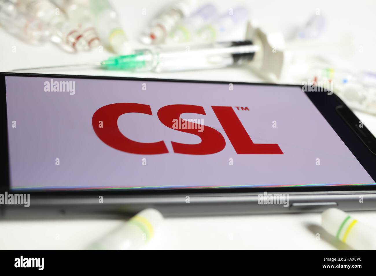 Viersen, Germania - Dicembre 1. 2021: Primo piano dello schermo del telefono cellulare con la scritta con il logo di CSL Behring, fiale per siero e sfondo della siringa (selettivo Foto Stock