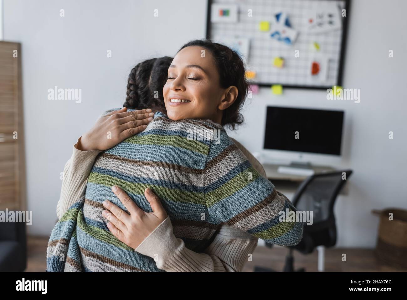felice madre afroamericana con occhi chiusi abbraccia la figlia teen in casa Foto Stock