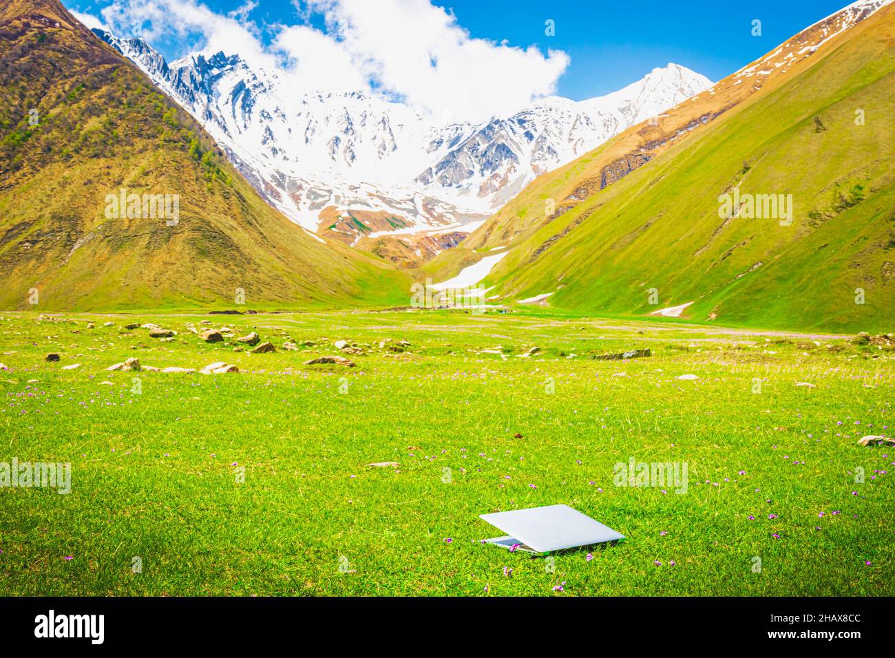taccuino bianco con coperchio chiuso sull'erba con montagne sullo sfondo e nessuna persona. tecnologie e lavoro remoto durante le vacanze Foto Stock