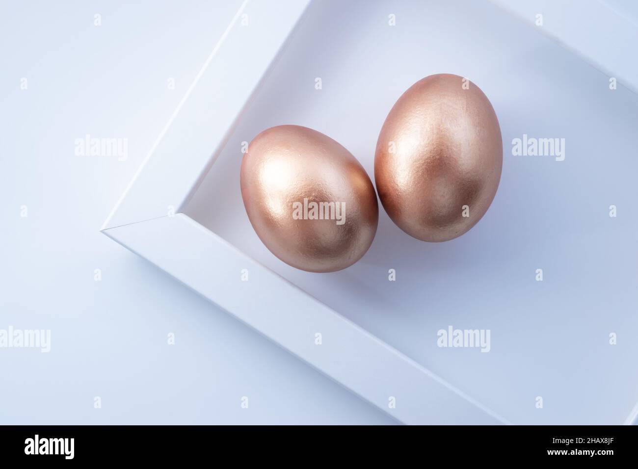 Coppia di uova d'oro pasquali con cornice geometrica su sfondo bianco. Composizione Pasqua minimalista. Disposizione piatta, vista dall'alto, spazio di copia Foto Stock