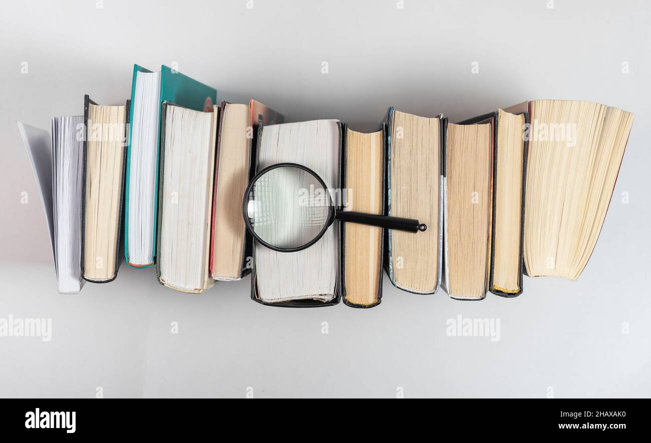 Lente di ingrandimento sulla riga dei libri. Concetto di conoscenza e studio. Foto Stock
