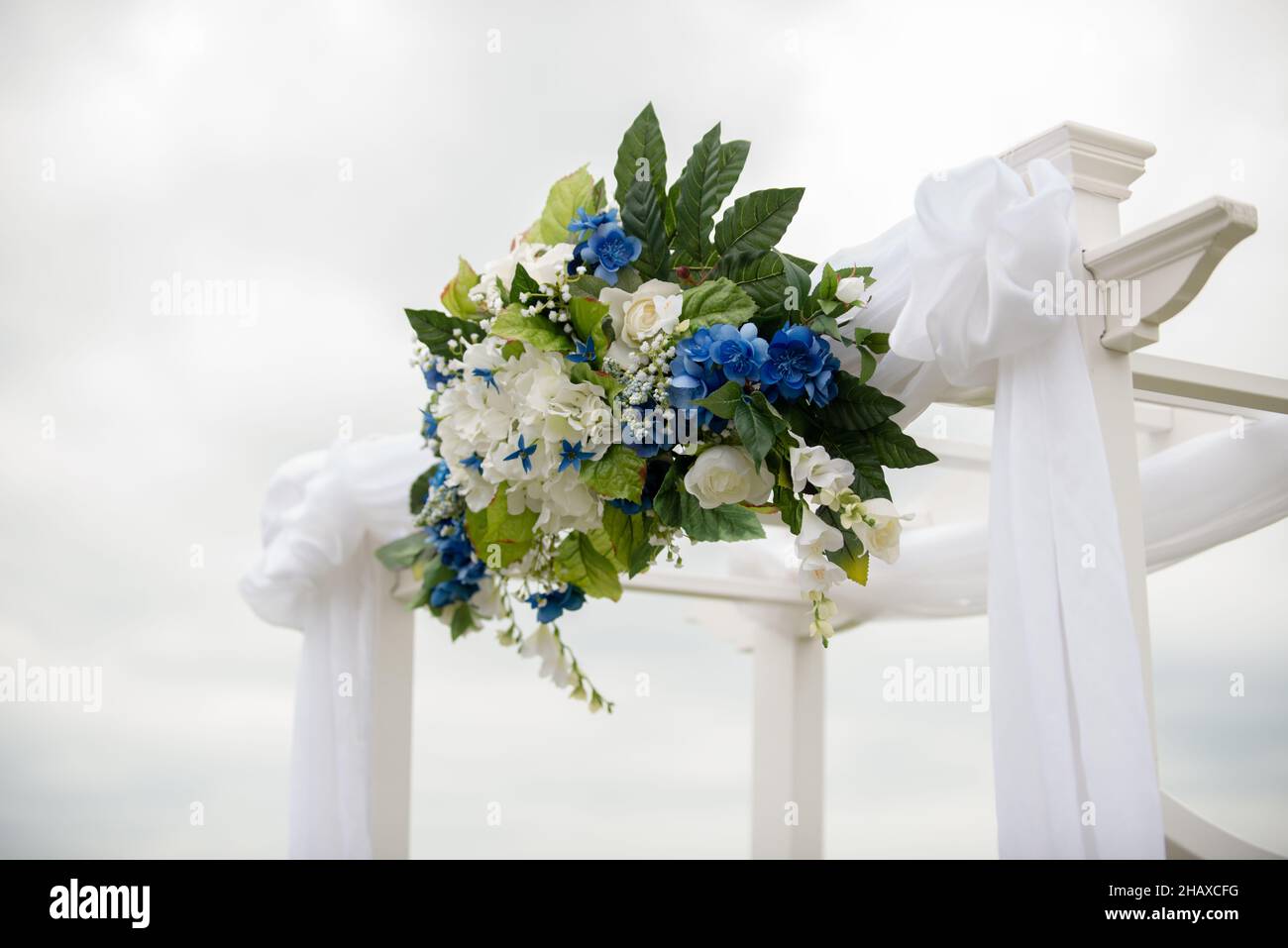 cerimonia di nozze bianco arco drappeggiato in tessuto bianco e decorato con fiori bianchi e blu Foto Stock