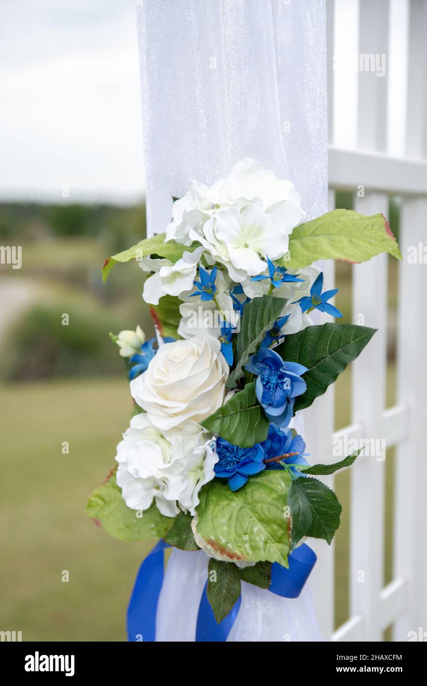 cerimonia di nozze bianco arco drappeggiato in tessuto bianco e decorato con fiori bianchi e blu Foto Stock