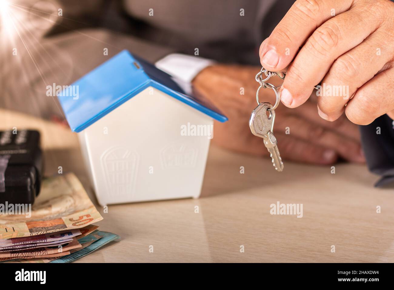 Uomo d'affari che tiene la chiave con la piccola casa sul tavolo. Concetto di alloggiamento. Foto Stock