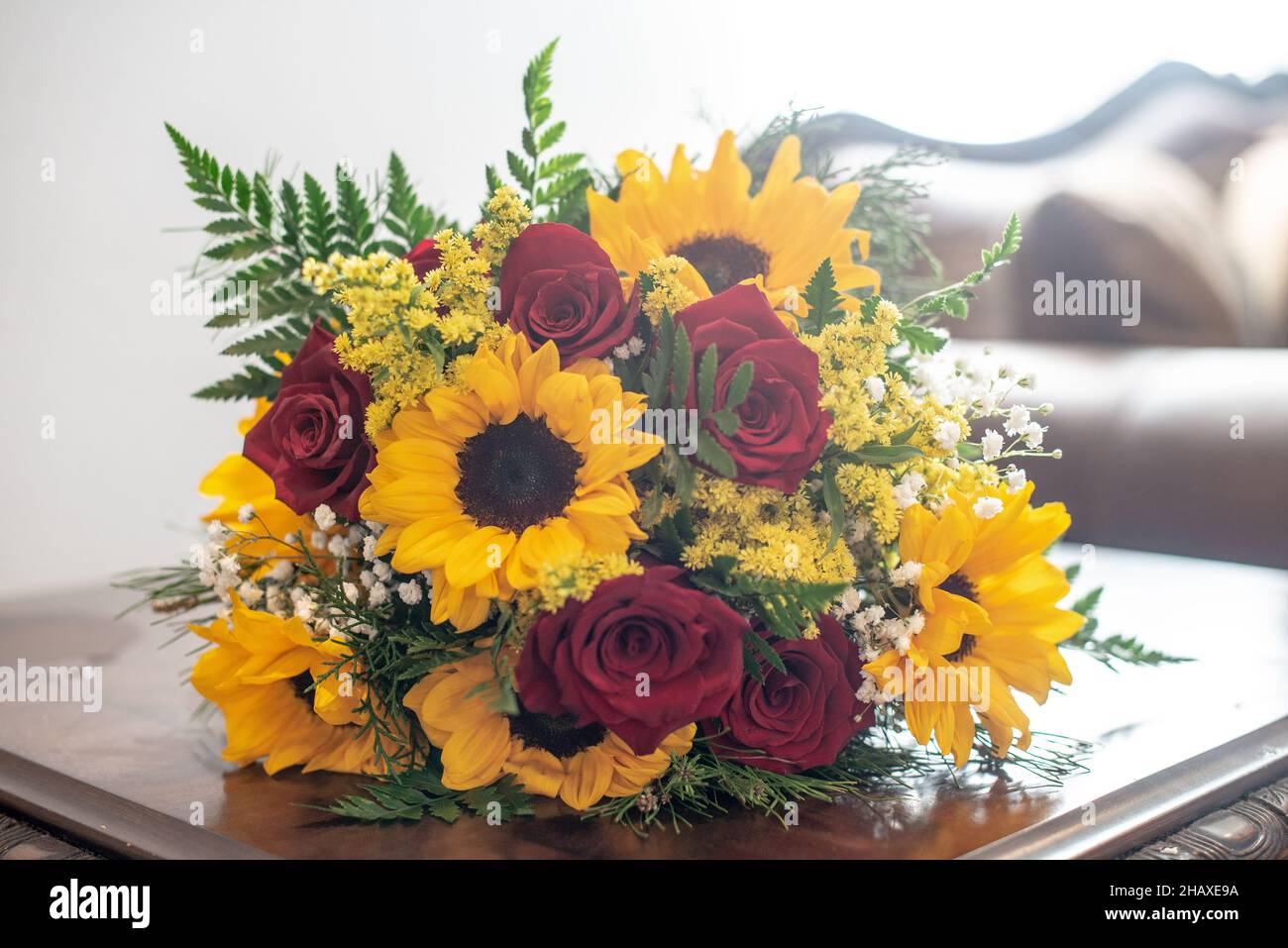 Bellissimi mazzi di girasoli e rose rosse sul tavolo di legno Foto Stock