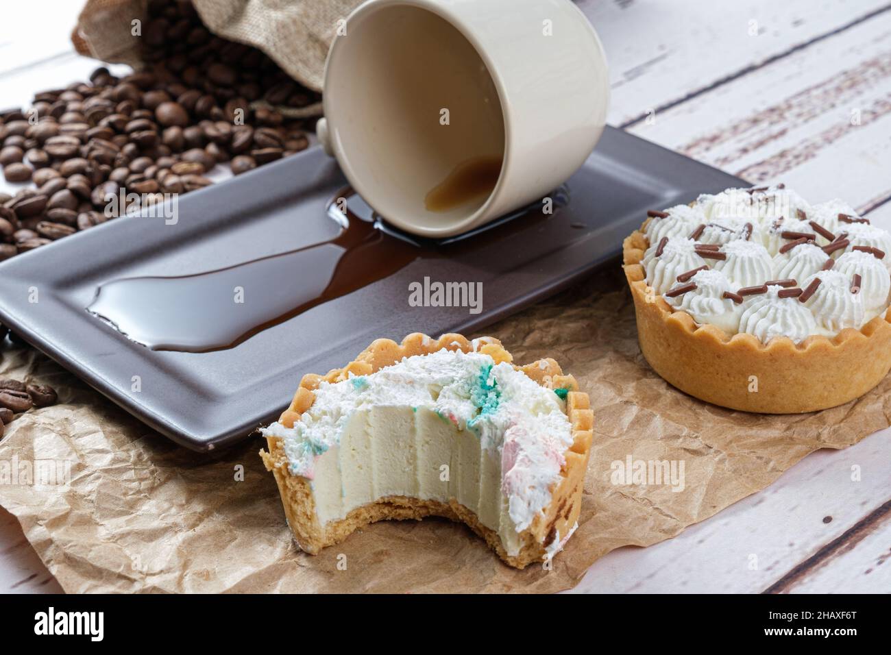 Mini torta con pasticceria e ganache di cioccolato bianco con un boccone, accanto a una tazza capovolta di caffè. Foto Stock