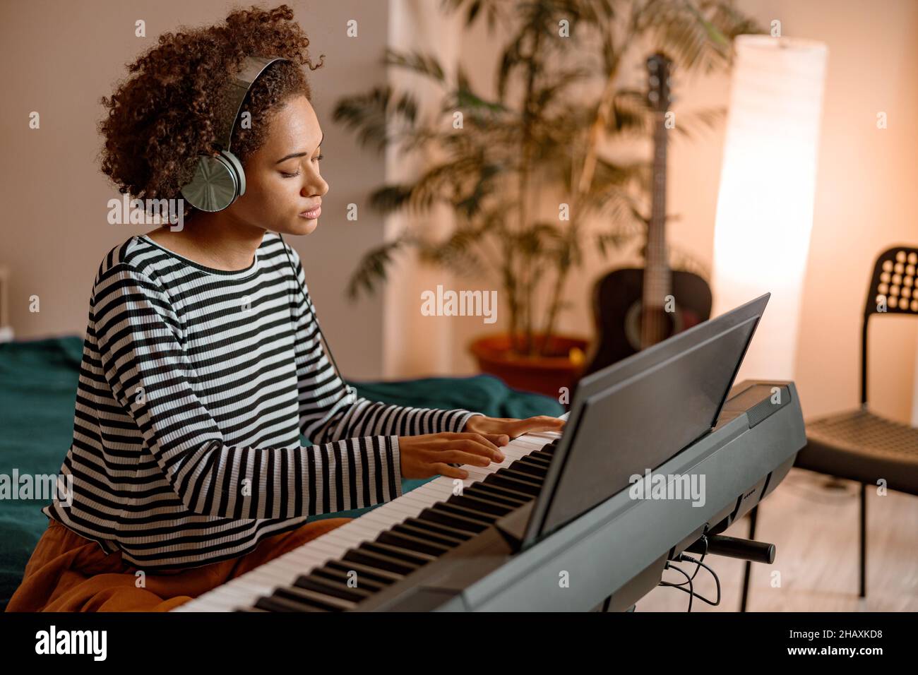 Giovane donna in cuffia che suona il sintetizzatore a casa Foto Stock