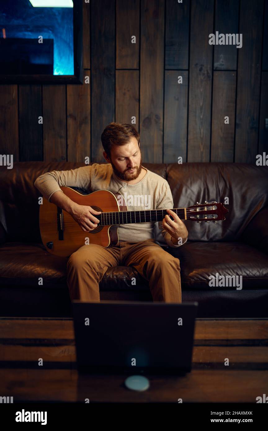 Giovane uomo che impara a suonare la chitarra attraverso internet Foto Stock