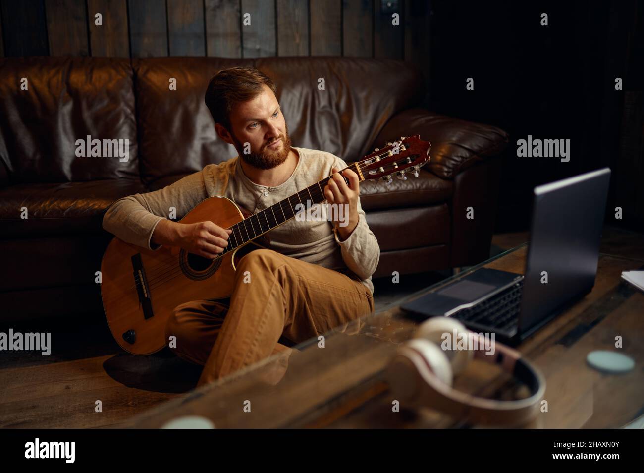 Uomo che suona la chitarra mentre guarda il laptop Foto Stock