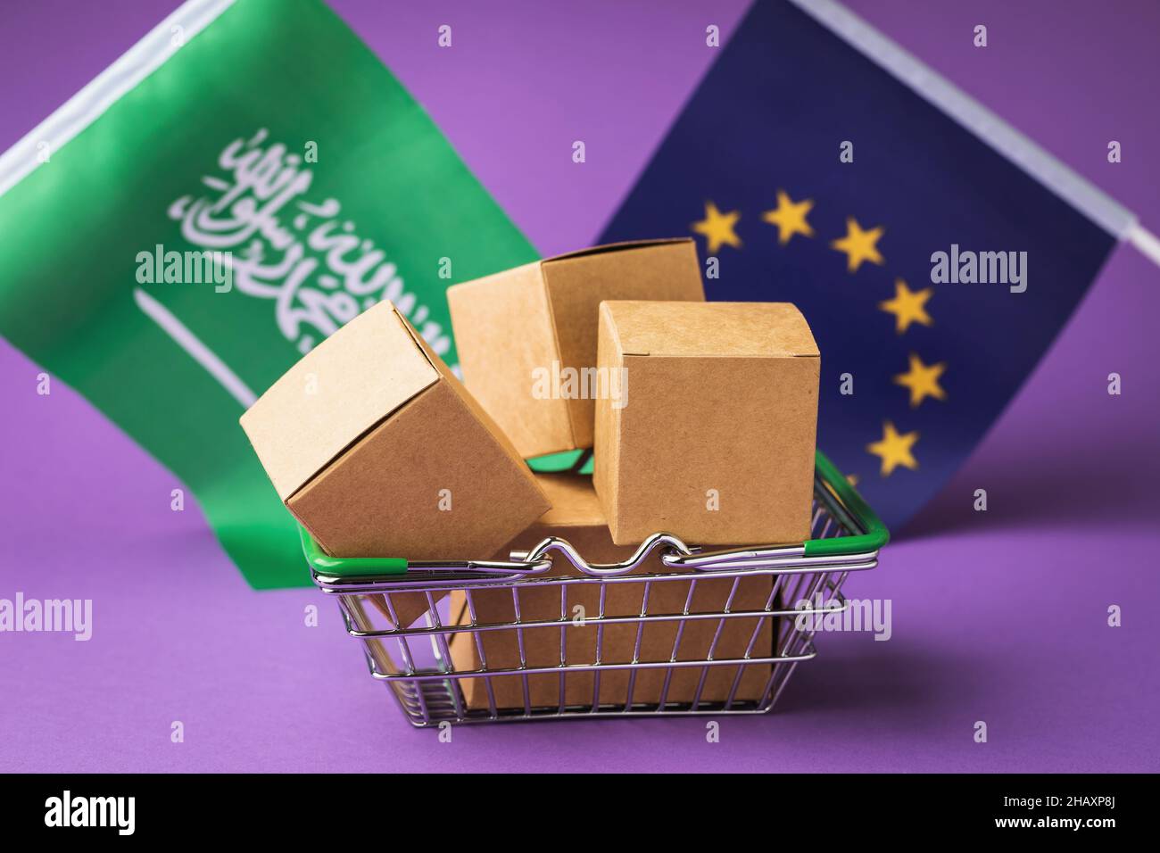 Scatole di cartone in un cestino alimentare e bandiere su sfondo colorato, il concetto di commercio tra l'UE e l'Arabia Saudita Foto Stock