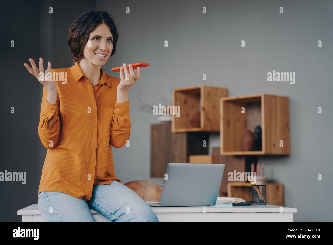 Felice dipendente ispanico che utilizza il vivavoce o un assistente vocale virtuale sul telefono cellulare Foto Stock