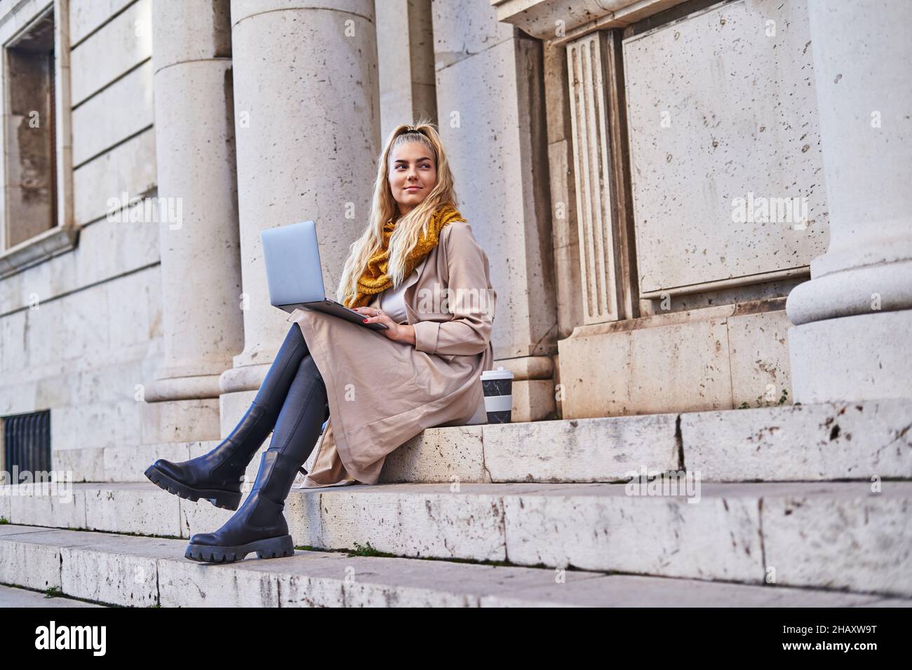Libera professionista femminile in casual vestito caldo controllare e-mail in notebook mentre si siede sulle scale dell'edificio Foto Stock