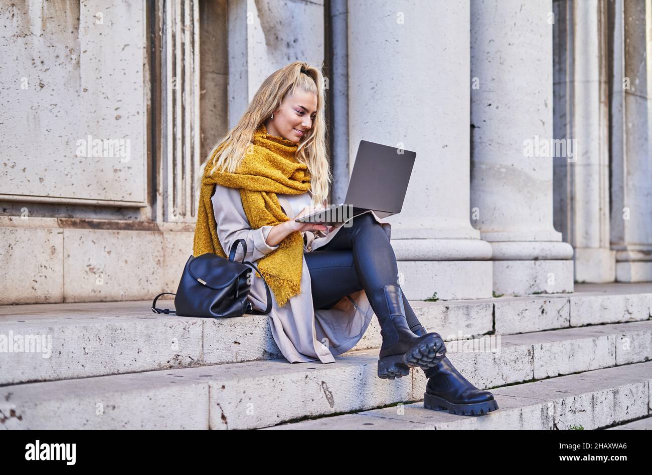 Libera professionista femminile in casual vestito caldo controllare e-mail in notebook mentre si siede sulle scale dell'edificio Foto Stock