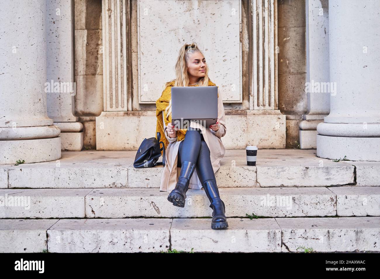 Libera professionista femminile in casual vestito caldo controllare e-mail in notebook mentre si siede sulle scale dell'edificio Foto Stock