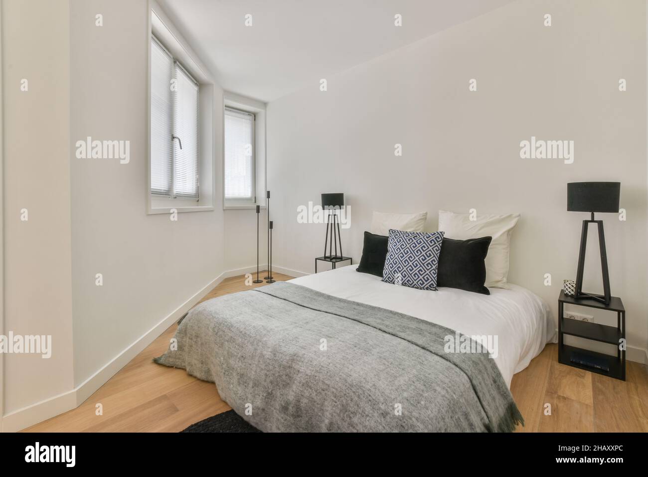 Confortevole camera da letto con letto coperto e coperta sotto cuscini comodini con lampade moderne Foto Stock
