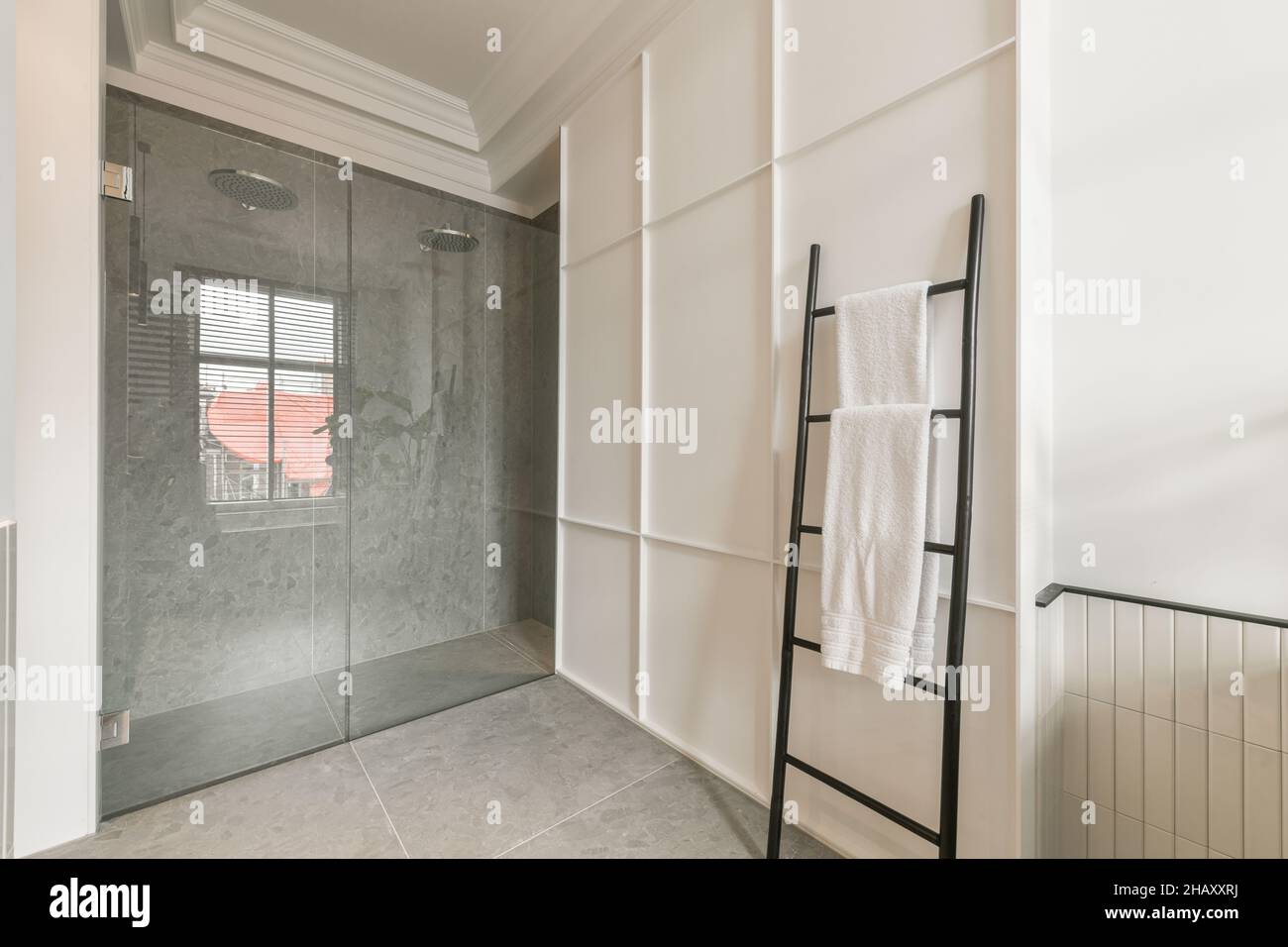 Bagno con cabina doccia doppia con annaffiatoi e pareti piastrellate e stand con morbidi asciugamani bianchi Foto Stock