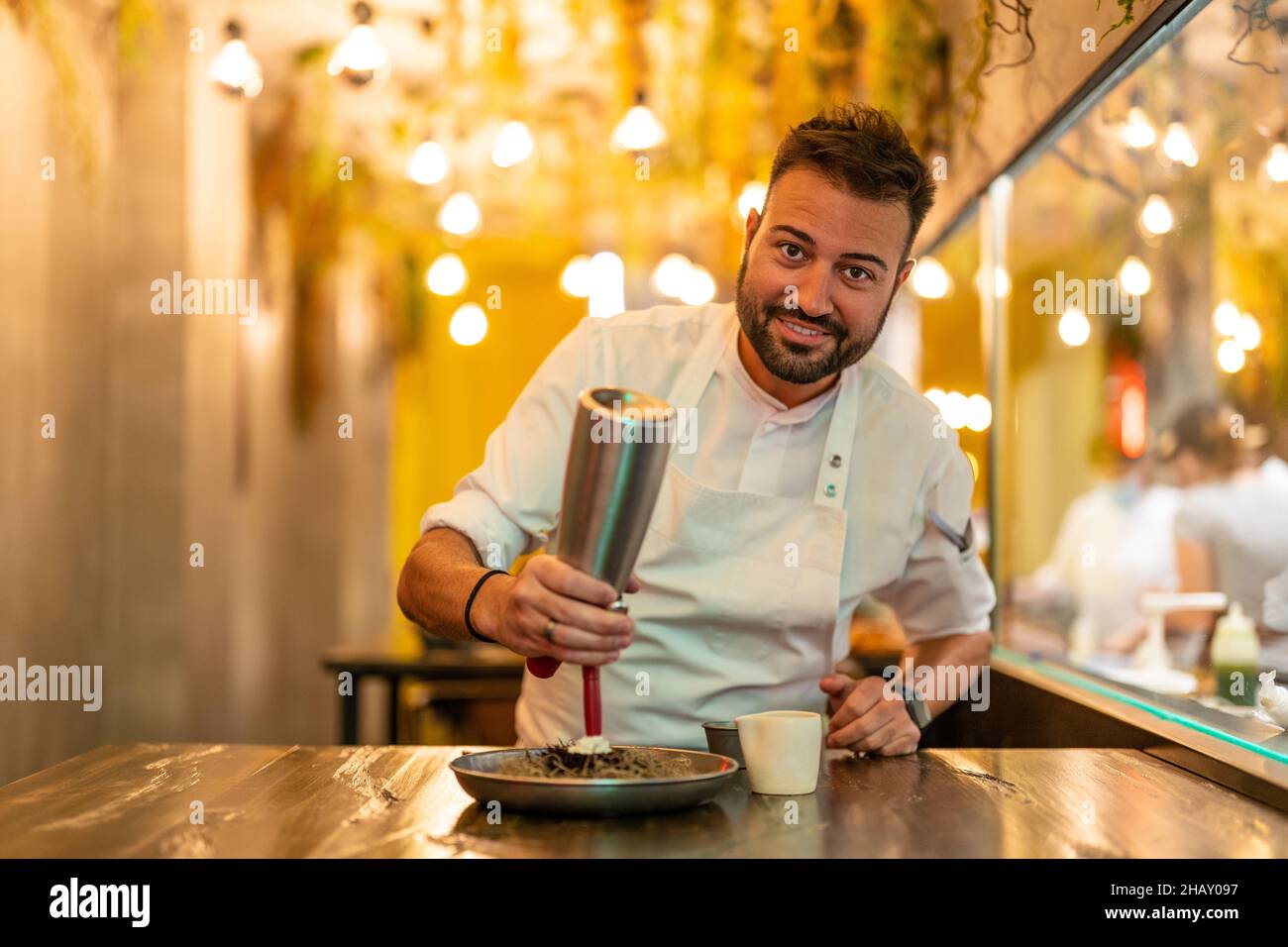 Chef professionista in uniforme bianca con dispenser che aggiunge crema su una porzione di riccio di mare gourmet in un ristorante con piatti raffinati Foto Stock