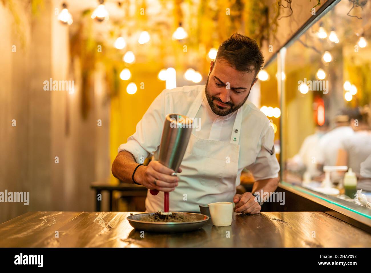 Chef professionista in uniforme bianca con dispenser che aggiunge crema su una porzione di riccio di mare gourmet in un ristorante con piatti raffinati Foto Stock
