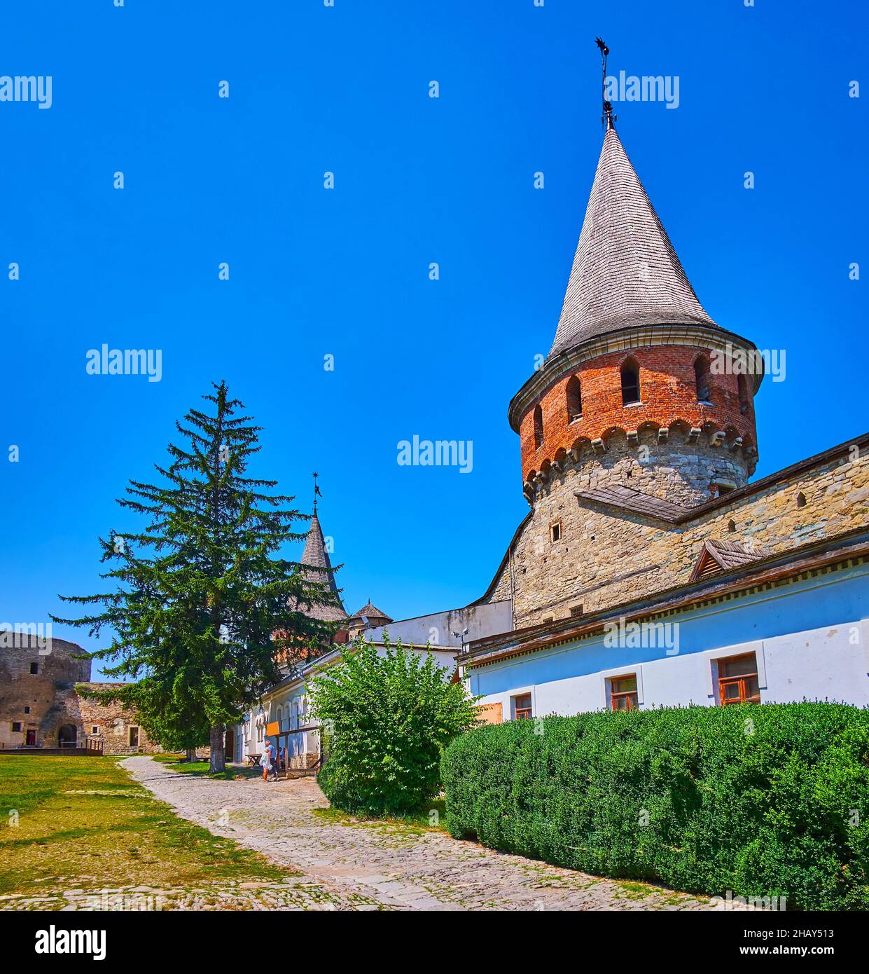 Il verde lussureggiante di fronte alle mura e il tetto conico Lanckoronska Torre del Castello Kamianets-Podilskyi, Ucraina Foto Stock