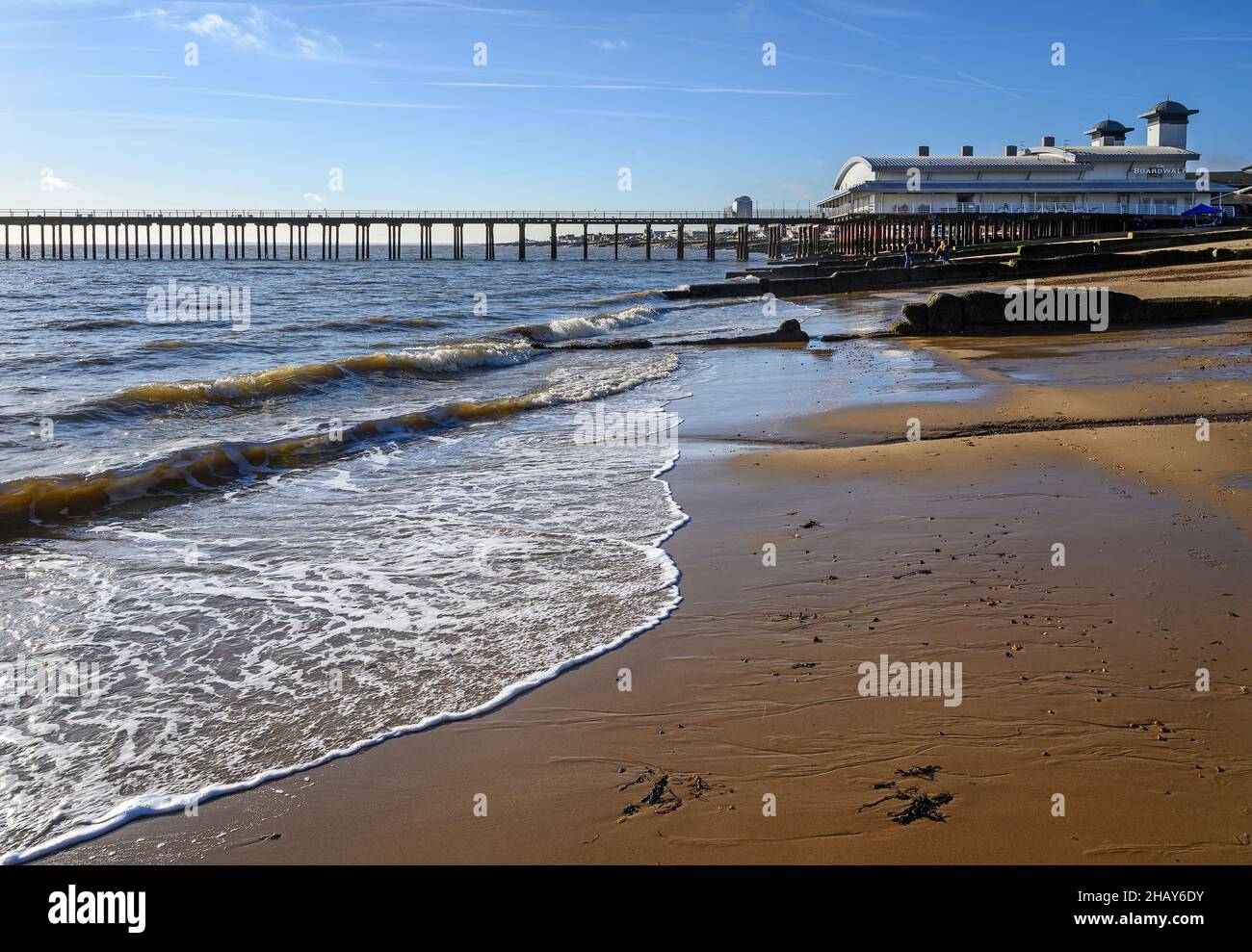 Felixstowe, Suffolk, Regno Unito: Le onde si infrangono contro la spiaggia sabbiosa nella località turistica inglese di Felixstowe con il molo alle spalle. Foto Stock