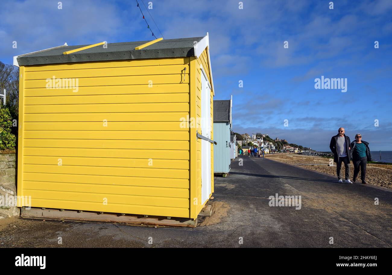 Felixstowe, Suffolk, Regno Unito : due persone camminano lungo la passeggiata nel villaggio turistico inglese di Felixstowe. Guardano ad una capanna di spiaggia di giallo chiaro. Foto Stock