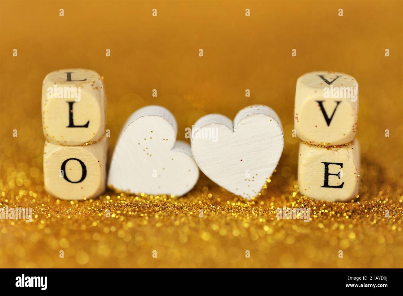 San Valentino. Amore e relazione. Iscrizione amore fatto di lettere in legno e cuori bianchi su uno sfondo oro glitter con bokeh d'oro Foto Stock