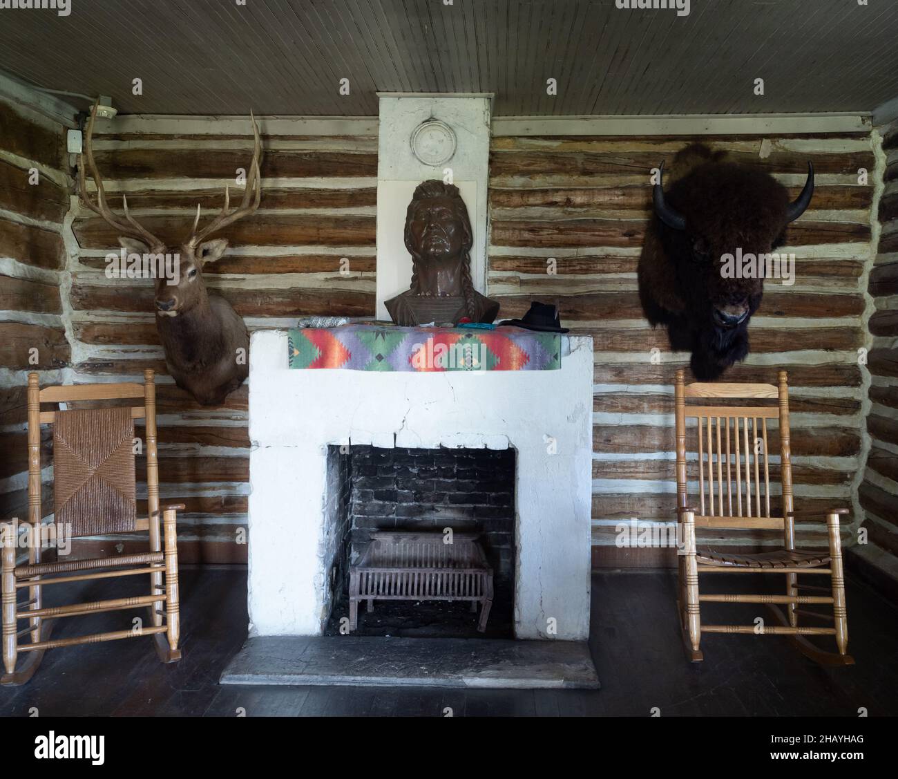 Interno del capo seduta Bull salotto con camino, sedie a dondolo, il suo busto, e la fauna selvatica supporti appesi sulla parete di legno. Foto Stock