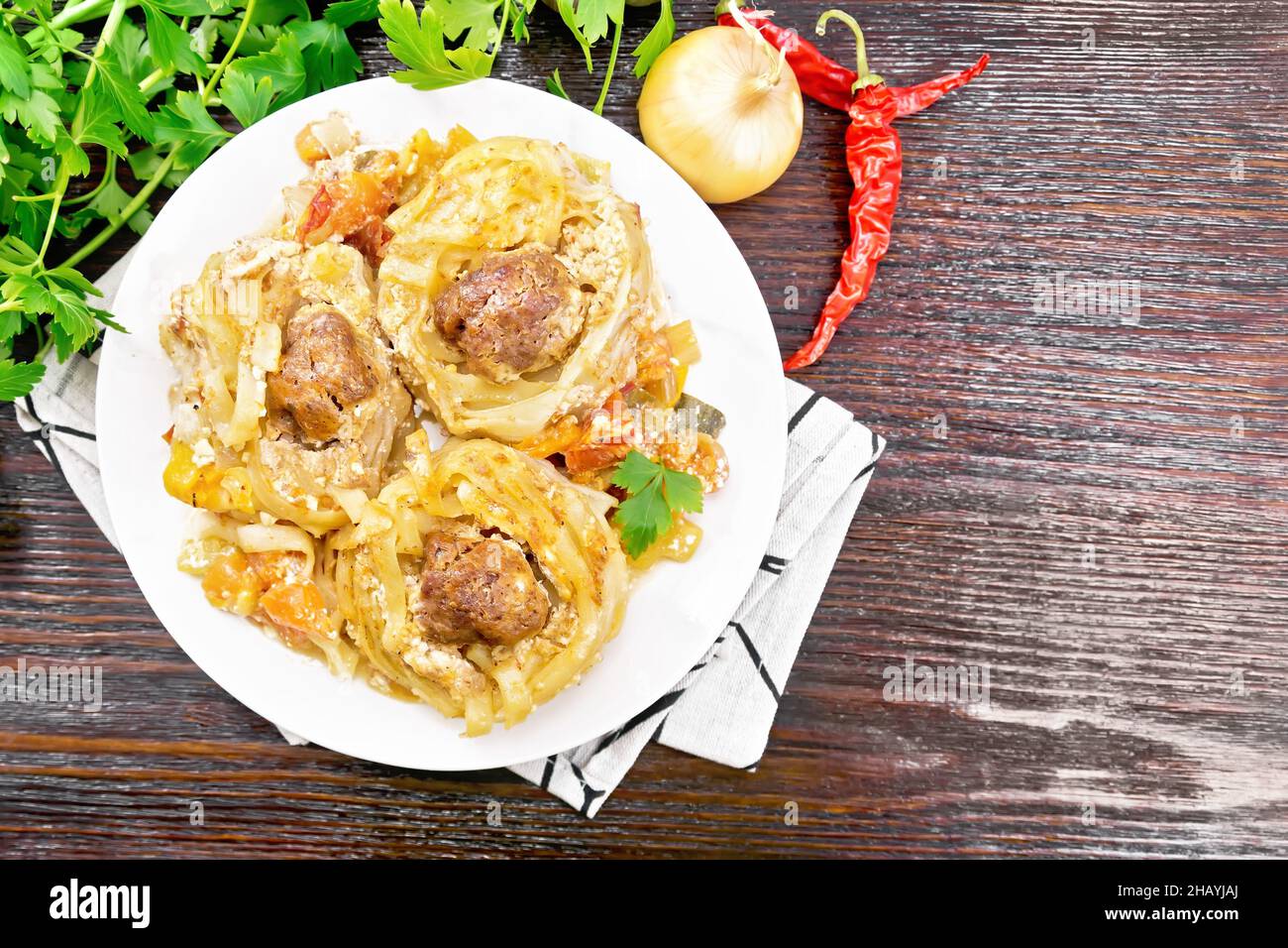 Pasta intrecciata con polpette al centro con salsa di panna, pomodori stufati, peperoni, cipolle e aglio in piatto bianco su tavola di legno backgroun Foto Stock