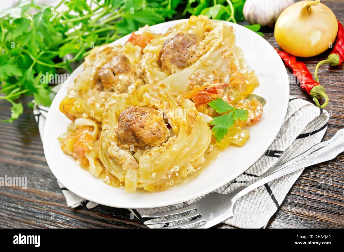Pasta intrecciata con polpette al centro con salsa di panna, pomodori stufati, peperoni, cipolle e aglio in piatto su un tovagliolo su tavola di legno bac Foto Stock