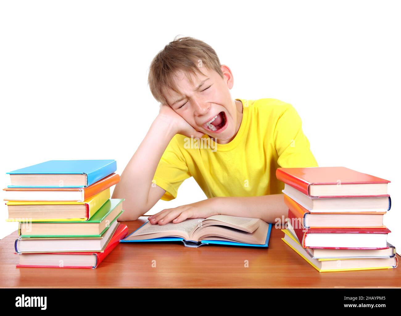 Il Kid stanco sbadiglio alla scrivania della scuola con un libro su sfondo bianco Foto Stock