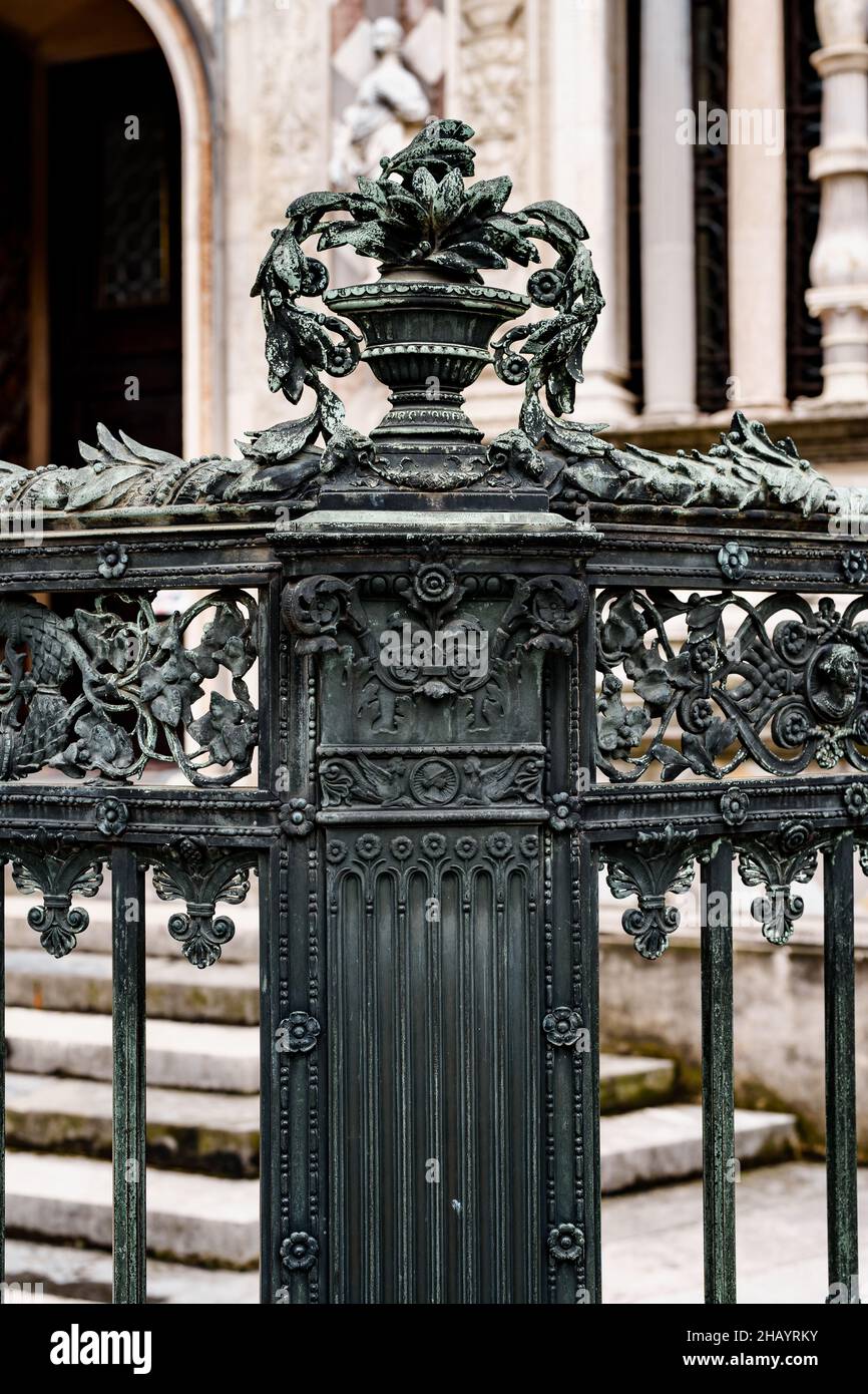 Vaso in metallo con fiori sul piedistallo di una vecchia recinzione in ferro battuto Foto Stock