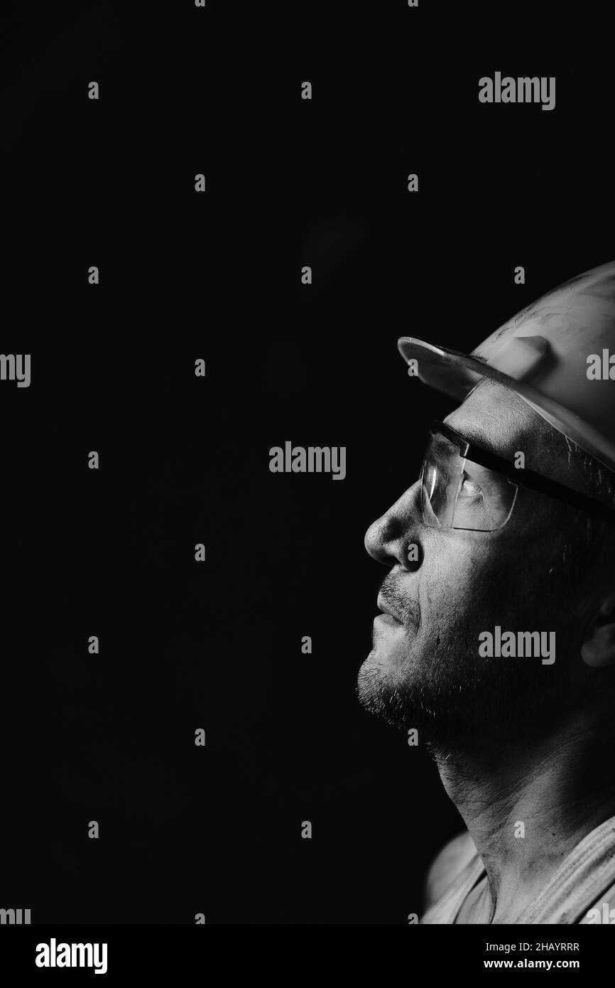Ritratto del profilo di un minatore in un casco e occhiali, guardando la luce.Un lavoratore sporco in una camicia. Foto Stock