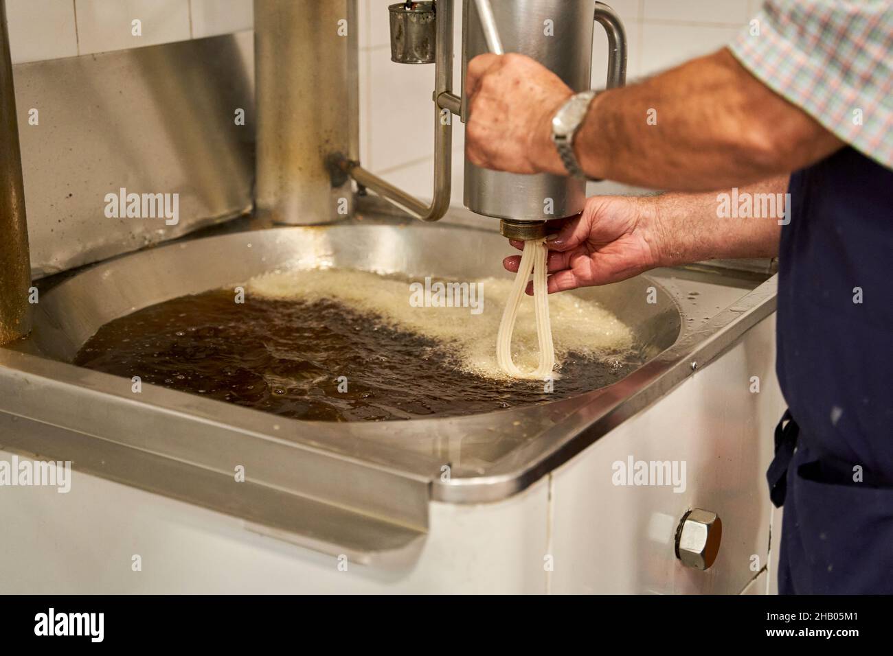 Vista laterale di un cuoco non identificato in grembiule versare l'impasto crudo in olio fritto mentre si preparano churros, tipica colazione spagnola. Foto Stock