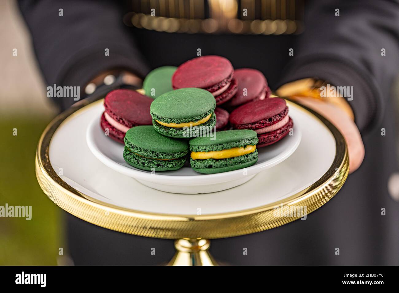 Mano femminile che serve macaron francesi colorati su un supporto per torte Foto Stock