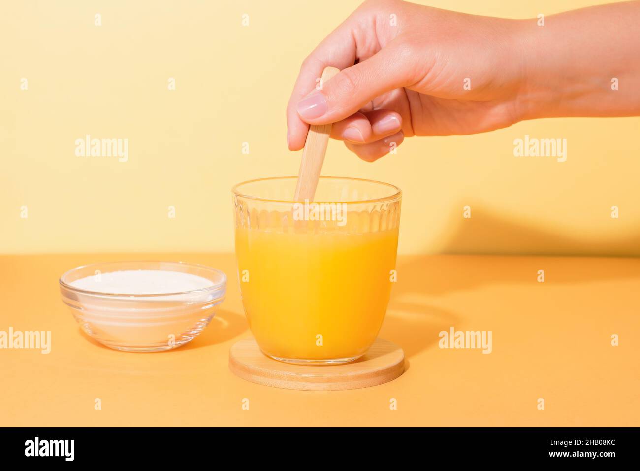 Bicchiere di succo d'arancia e polvere di collagene sul tavolo con pianta in luce dura. Composizione luminosa e minimale con ombre dure su sfondo colorato. Donna Foto Stock