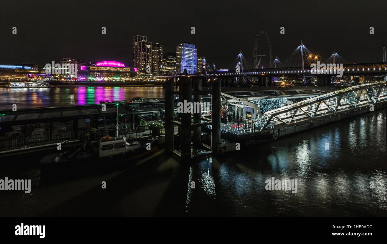 Insuale per vedere il London Eye nelle tenebre mentre il resto di Londra è illuminato di colore. Foto Stock