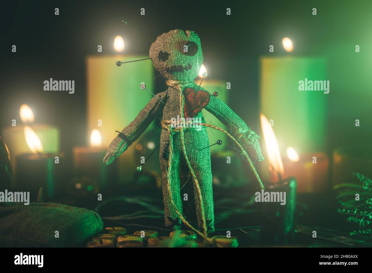 Voodoo Doll con luce verde drammatica al buio tra le candele. Foto Stock