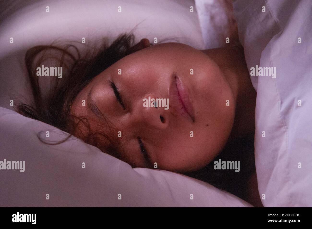 Una bella donna di razza mista (1/2 birmana, 1/4 laotiana e 1/4 cambogiana) che dorme a letto con luce mattutina che illumina il viso in una camera d'albergo. Siem Reap, Cambogia. © Kraig Lieb Foto Stock