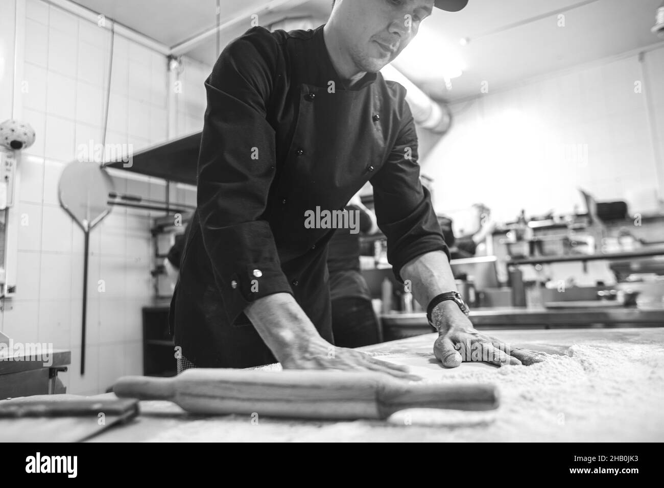 Cucina professionale nel ristorante dell'hotel, preparando la cena. Un cuoco in grembiule fa una pizza. L'uomo rotola fuori l'impasto della pizza Foto Stock