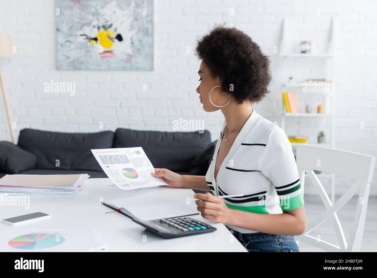 Donna afroamericana che guarda le carte in prossimità di calcolatrice e smartphone a casa Foto Stock