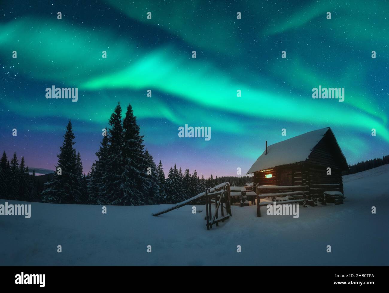 Fantastico paesaggio invernale con casa in legno con luce nella finestra in montagne innevate e northen luce nel cielo notturno. Vacanze di Natale e le vacanze invernali concept Foto Stock