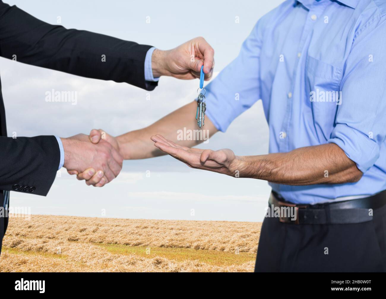 Metà sezione di agente immobiliare che dà le chiavi ad un uomo contro campo di erba e cielo blu Foto Stock