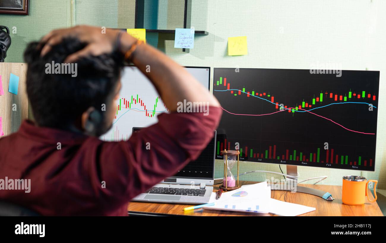 Focus su Monitor, giovane uomo deluso per la strategia fallita di trading mentre si guarda Graph su computer in ufficio a casa - concetto di investimento di denaro Foto Stock
