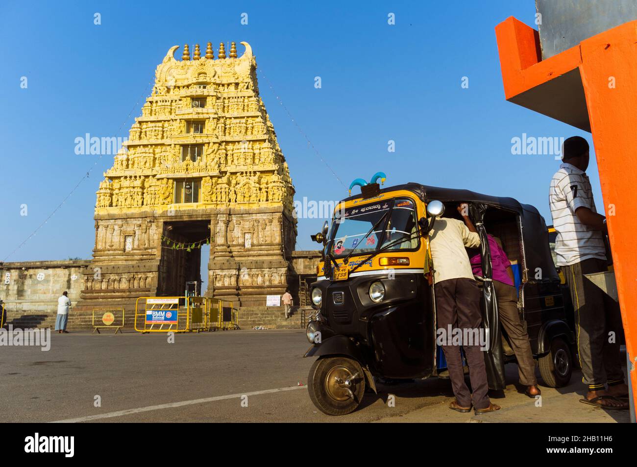 Belur, Karnataka, India : un gruppo di uomini si trova accanto ad un auto-risciò accanto alla porta del gopuram del Tempio di Cheannakeshava. Foto Stock