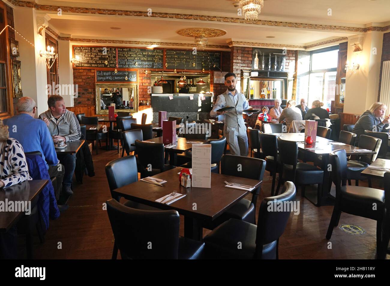 Un cameriere trasporta i pasti ad alcuni dei pochi clienti che mangiano al ristorante Cassia Sambuca a North Shields, North Tyneside, che normalmente sarebbe imballato con i clienti che approfittano delle specialita' dell'ora di pranzo. Le aziende del settore alberghiero stanno aumentando le richieste di sostegno da parte del governo per i pub e i ristoranti di grande successo, mentre la variante Omicron spazza il paese e la fiducia dei consumatori è abbattuta da nuove restrizioni e crescenti avvertenze sulla salute. Data immagine: Giovedì 16 dicembre 2021. Foto Stock